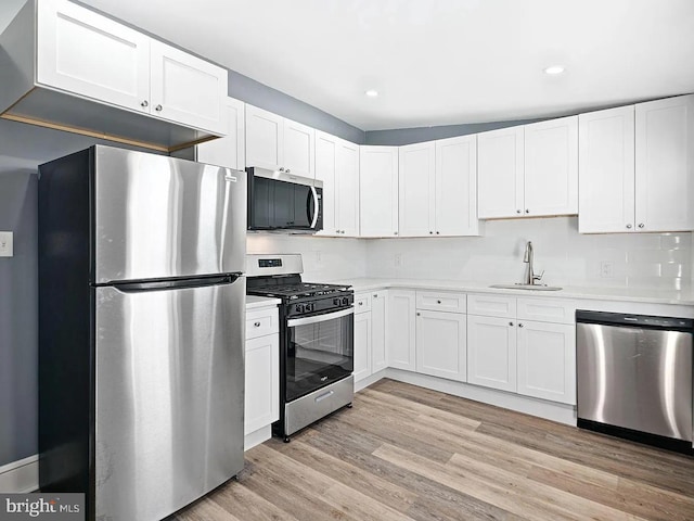 kitchen featuring stainless steel appliances, light countertops, light wood-style floors, white cabinetry, and a sink