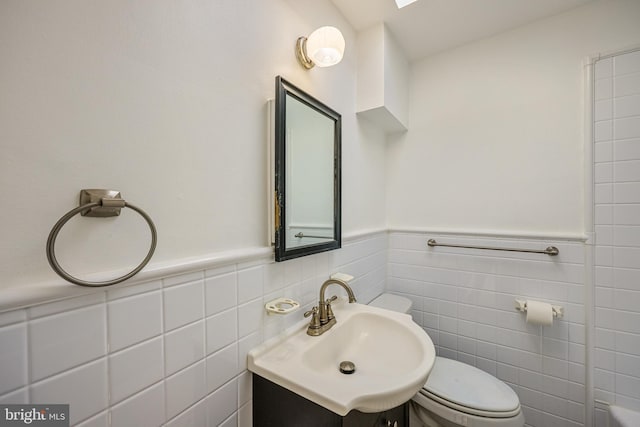 bathroom featuring a wainscoted wall, toilet, tile walls, and vanity