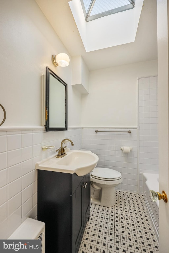 bathroom with vanity, a skylight, wainscoting, tile walls, and toilet