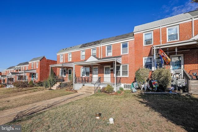 townhome / multi-family property featuring brick siding, a residential view, covered porch, and a front lawn