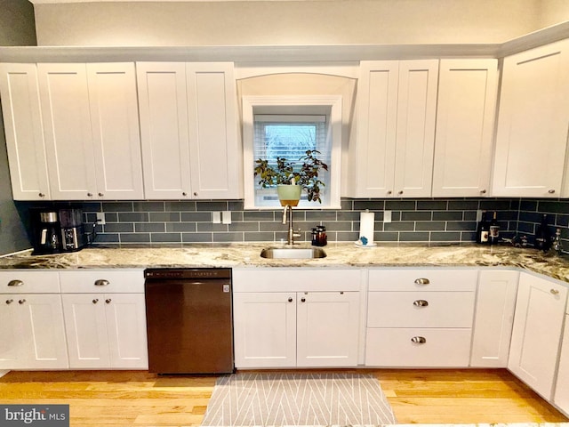 kitchen with light wood-style flooring, white cabinetry, black dishwasher, and a sink