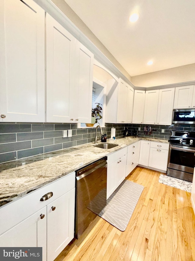 kitchen with light wood-type flooring, a sink, tasteful backsplash, white cabinetry, and stainless steel appliances