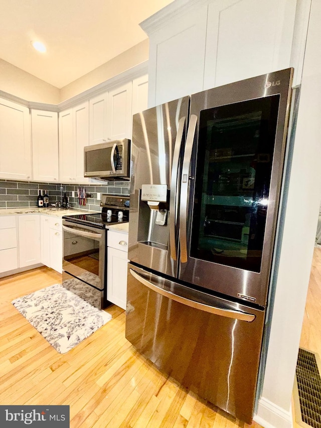 kitchen with tasteful backsplash, light wood-style floors, appliances with stainless steel finishes, white cabinets, and light countertops