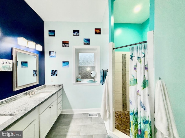 bathroom with visible vents, baseboards, double vanity, tiled shower, and a sink