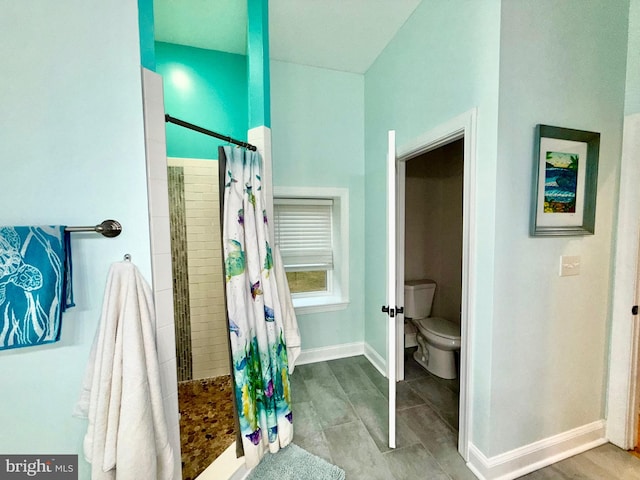 full bath featuring toilet, baseboards, and tiled shower