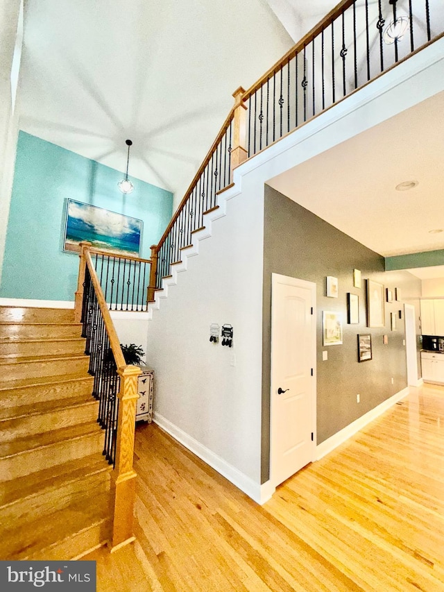 stairway with a towering ceiling, baseboards, and wood finished floors