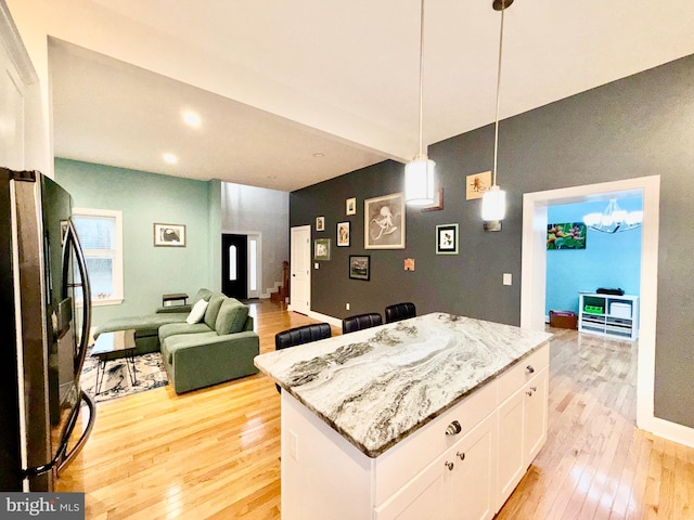 kitchen with light wood-style flooring, open floor plan, a center island, white cabinetry, and freestanding refrigerator