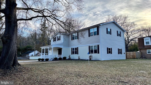 view of front facade featuring covered porch, a front lawn, and fence