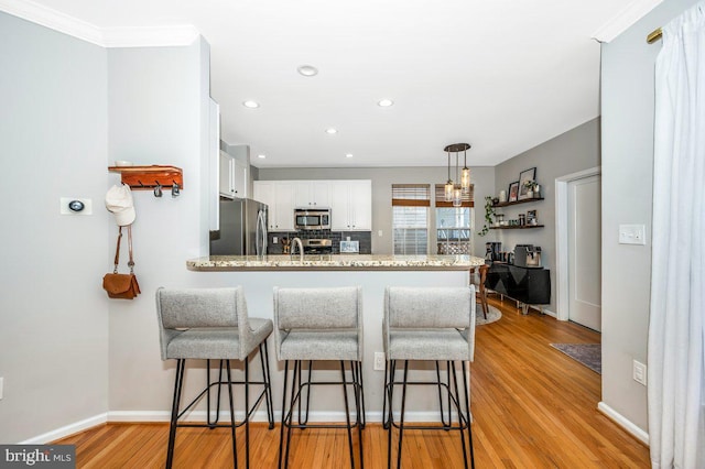 kitchen featuring light wood finished floors, tasteful backsplash, appliances with stainless steel finishes, a peninsula, and white cabinetry