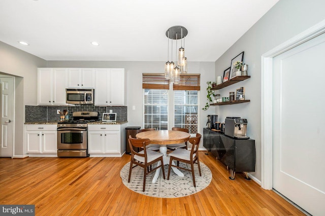 kitchen with a notable chandelier, stainless steel appliances, backsplash, white cabinets, and light wood-type flooring