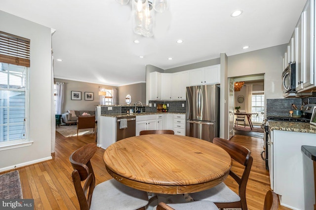 kitchen with light wood-style flooring, backsplash, a peninsula, stainless steel appliances, and a sink