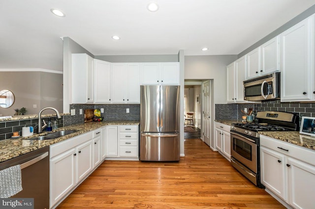 kitchen with appliances with stainless steel finishes, light wood-style floors, white cabinets, a sink, and dark stone counters