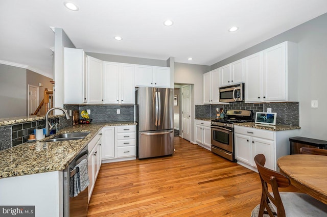 kitchen with stainless steel appliances, light wood-style flooring, white cabinetry, a sink, and dark stone countertops