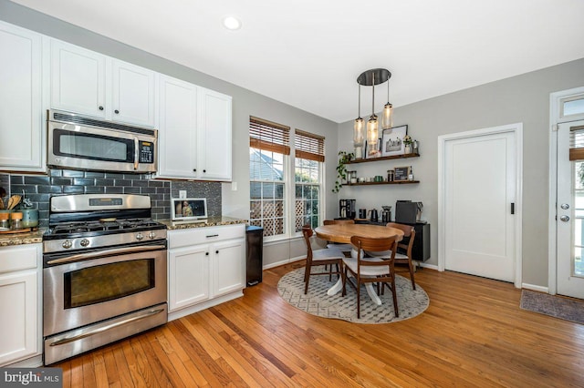 kitchen with pendant lighting, stainless steel appliances, white cabinetry, light wood finished floors, and tasteful backsplash