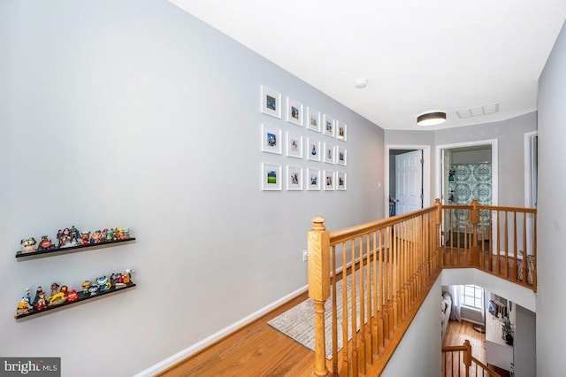 corridor featuring visible vents, baseboards, wood finished floors, and an upstairs landing