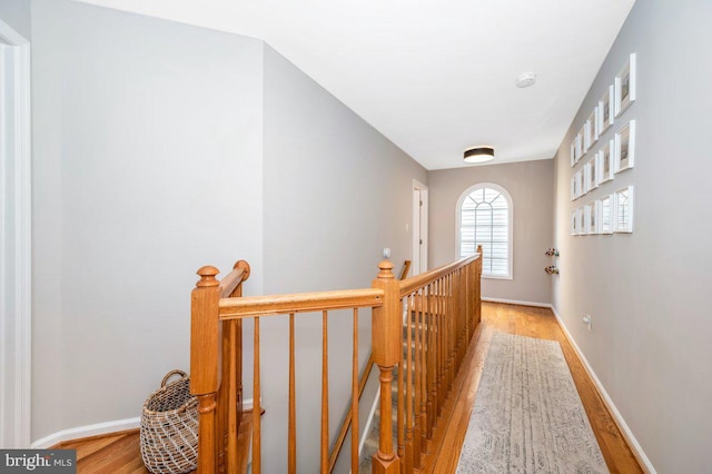 corridor with baseboards, wood finished floors, and an upstairs landing