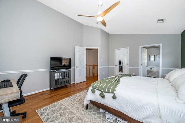 bedroom with baseboards, visible vents, ensuite bath, wood finished floors, and vaulted ceiling