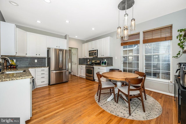 kitchen with stainless steel appliances, a sink, white cabinetry, and light wood-style floors