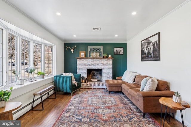 living area with wood-type flooring, visible vents, baseboard heating, and crown molding