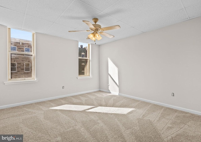 carpeted empty room with a drop ceiling, ceiling fan, and baseboards