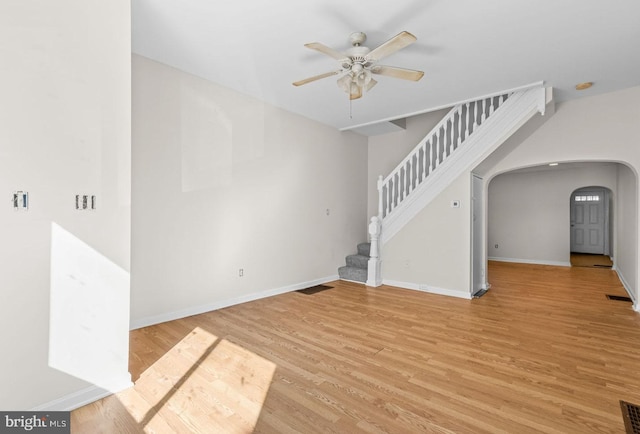 empty room featuring arched walkways, light wood finished floors, stairway, ceiling fan, and baseboards