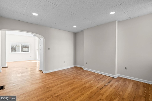 empty room with arched walkways, light wood finished floors, and baseboards