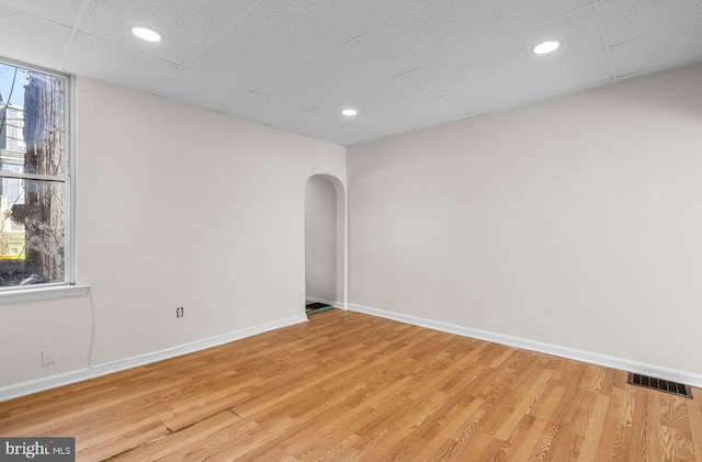 unfurnished room with light wood-style floors, plenty of natural light, visible vents, and arched walkways