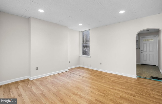 spare room featuring arched walkways, a drop ceiling, recessed lighting, baseboards, and light wood-type flooring