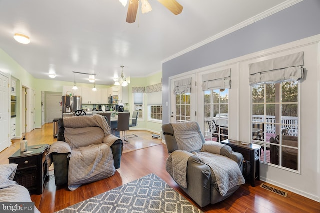 living room featuring ceiling fan, wood finished floors, visible vents, baseboards, and crown molding