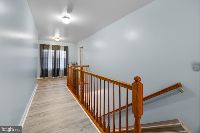 corridor with light wood-type flooring, baseboards, and an upstairs landing