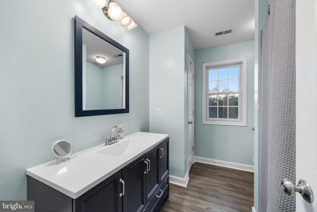 bathroom with visible vents, vanity, baseboards, and wood finished floors