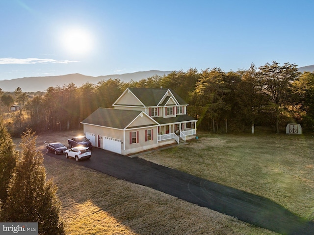 view of front of property featuring a garage, aphalt driveway, covered porch, a wooded view, and a front yard