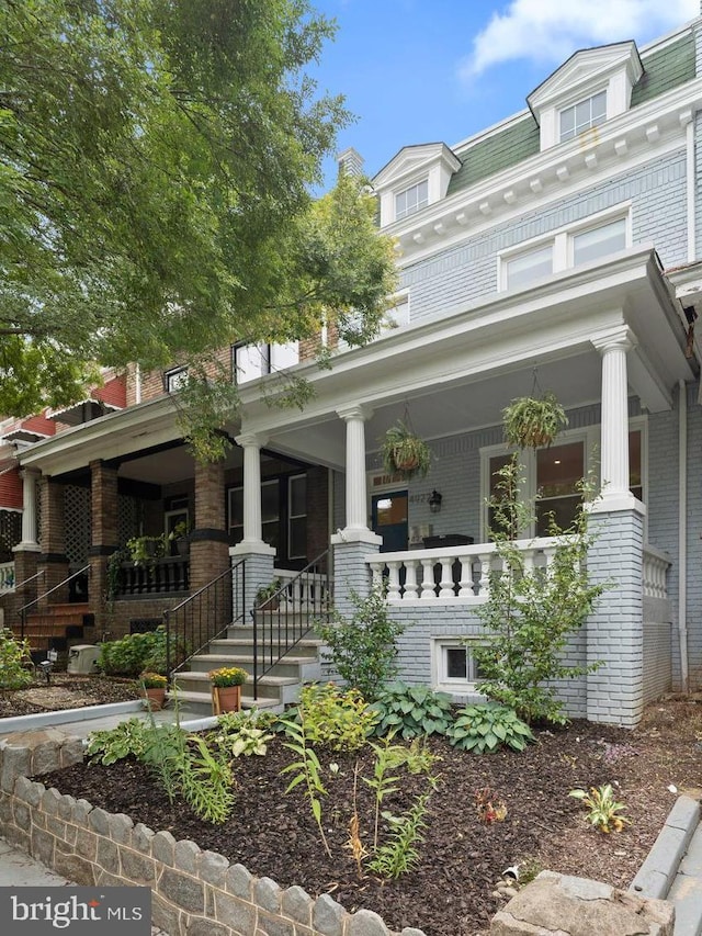 view of front of house featuring covered porch, mansard roof, and brick siding