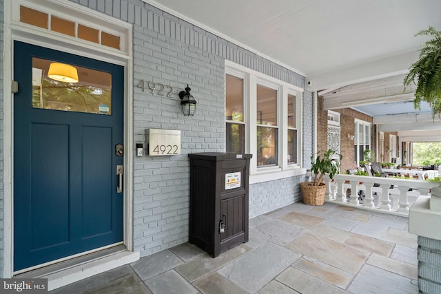 doorway to property featuring a porch and brick siding