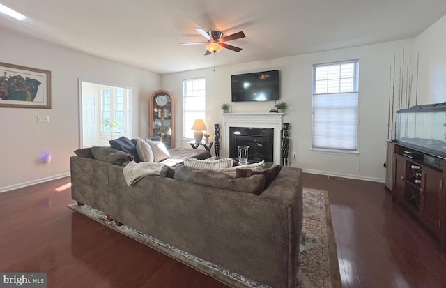 living area featuring a ceiling fan, baseboards, visible vents, dark wood-type flooring, and a glass covered fireplace