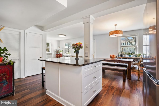 kitchen with a breakfast bar, dark stone countertops, dark wood-style floors, white cabinets, and ornate columns