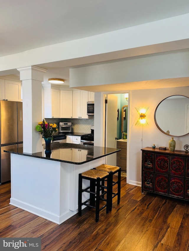 kitchen with a toaster, dark wood-style flooring, stainless steel appliances, white cabinets, and backsplash