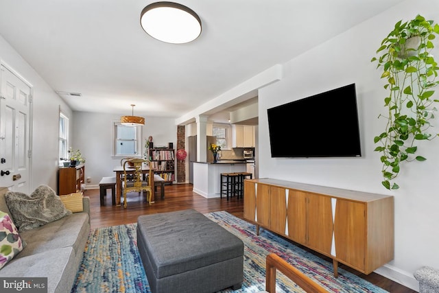 living room with dark wood-style floors, visible vents, baseboards, and decorative columns