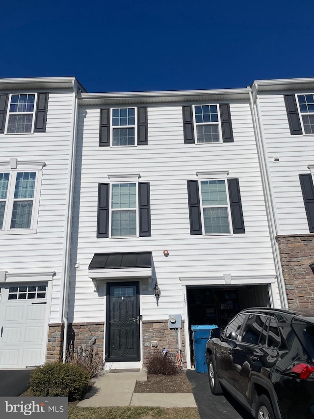 view of property featuring an attached garage, stone siding, and driveway