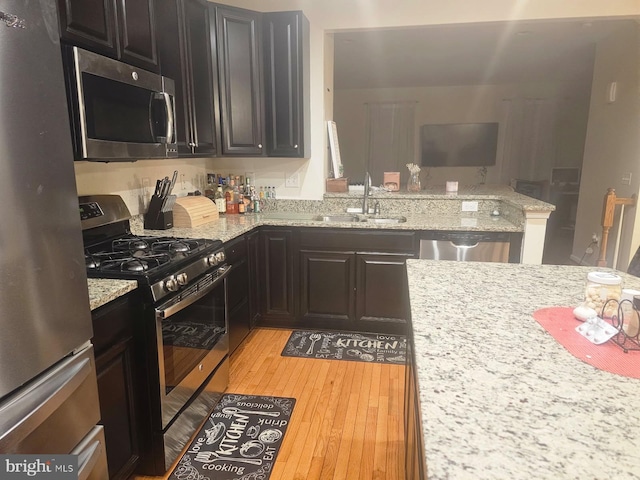 kitchen with light stone counters, a peninsula, a sink, appliances with stainless steel finishes, and light wood finished floors