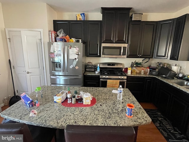 kitchen featuring light stone countertops, dark cabinets, a breakfast bar, appliances with stainless steel finishes, and a center island