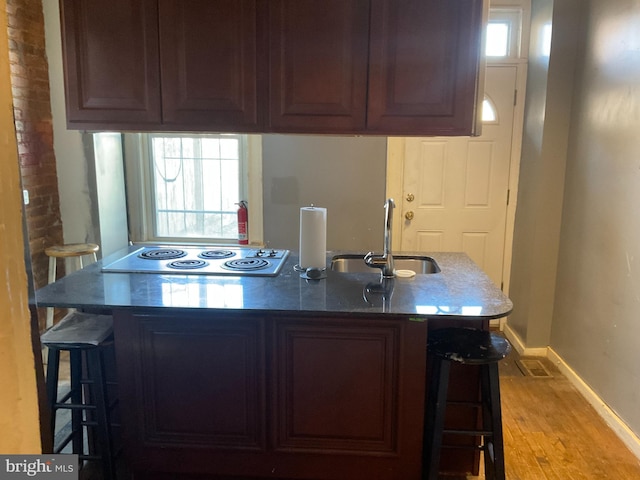 kitchen with a sink, a kitchen breakfast bar, wood finished floors, electric stovetop, and baseboards