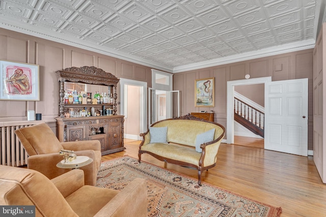 living room featuring light wood-style floors, an ornate ceiling, a decorative wall, and crown molding