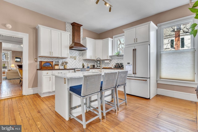 kitchen with light wood-style flooring, white cabinets, high end white fridge, and wall chimney range hood