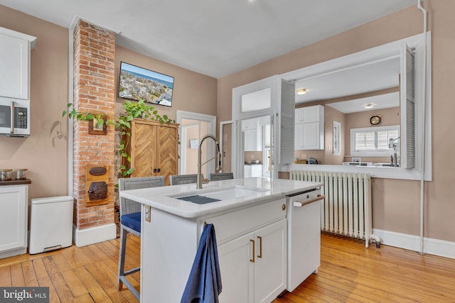 kitchen featuring stainless steel microwave, radiator heating unit, light wood-style floors, white cabinetry, and a sink