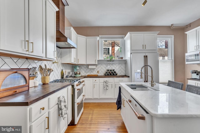 kitchen featuring white appliances, a sink, wall chimney range hood, and wood counters