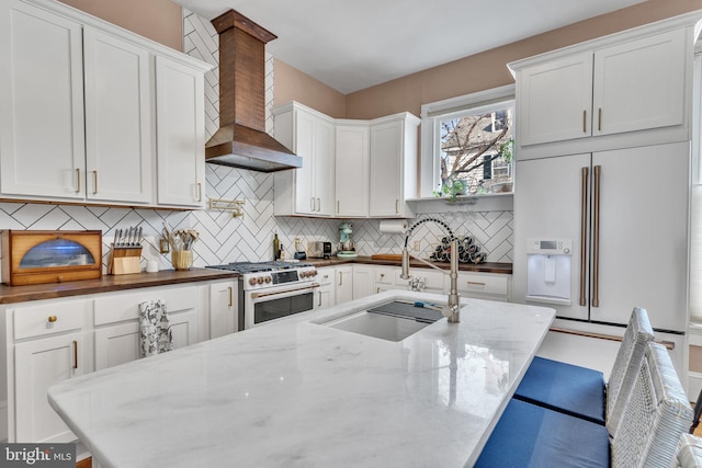 kitchen featuring tasteful backsplash, wall chimney exhaust hood, high quality appliances, white cabinetry, and a sink