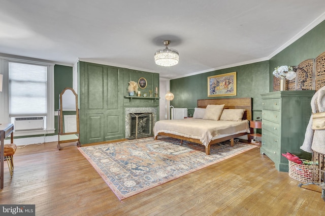 bedroom with light wood-type flooring, a fireplace, cooling unit, and crown molding