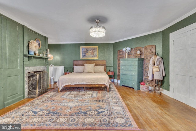 bedroom with ornamental molding, a large fireplace, baseboards, and wood finished floors