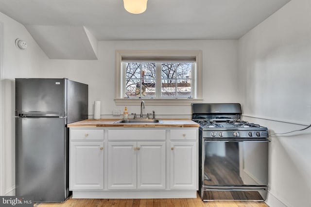 kitchen featuring wooden counters, black gas range oven, freestanding refrigerator, white cabinetry, and a sink